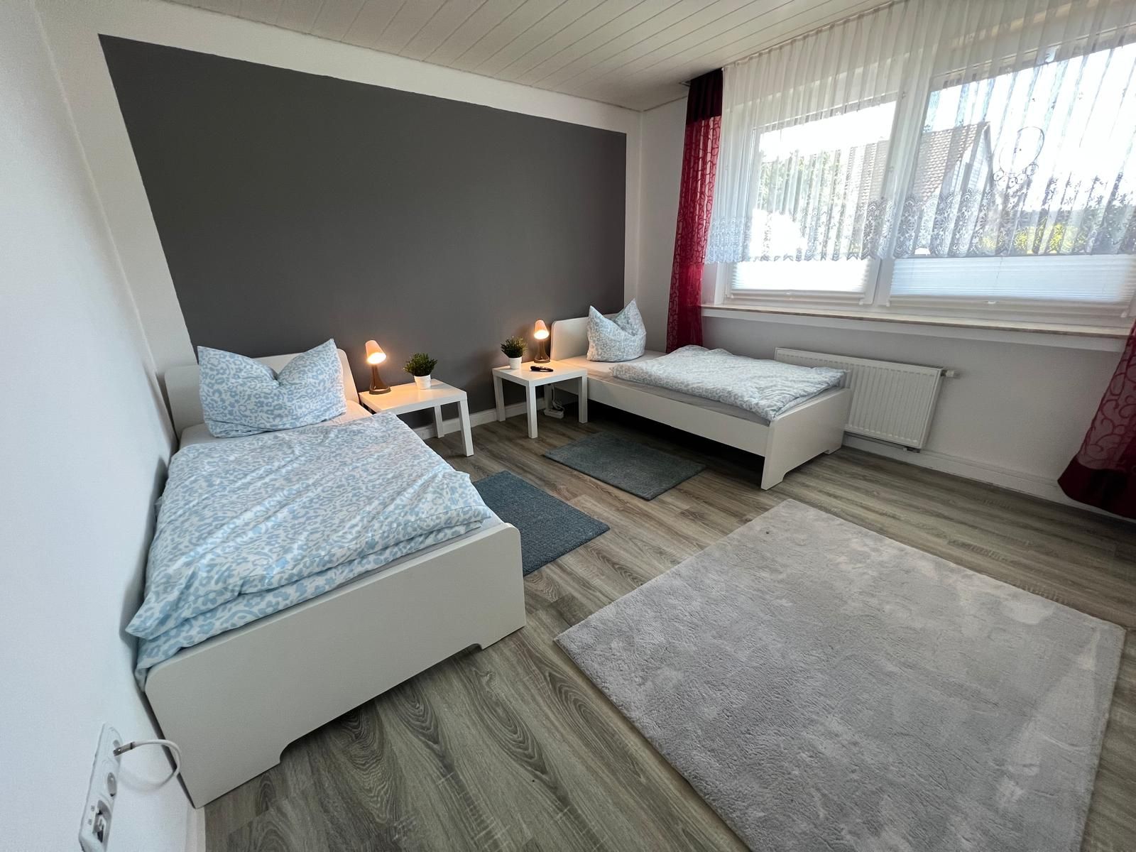 Ein hell ausgeleuchtetes, wohnlich wirkendes Zweibett-Schlafzimmer mit guten Möbeln, Vorhängen und durchdachtem Design — ideal für zwei Monteure.