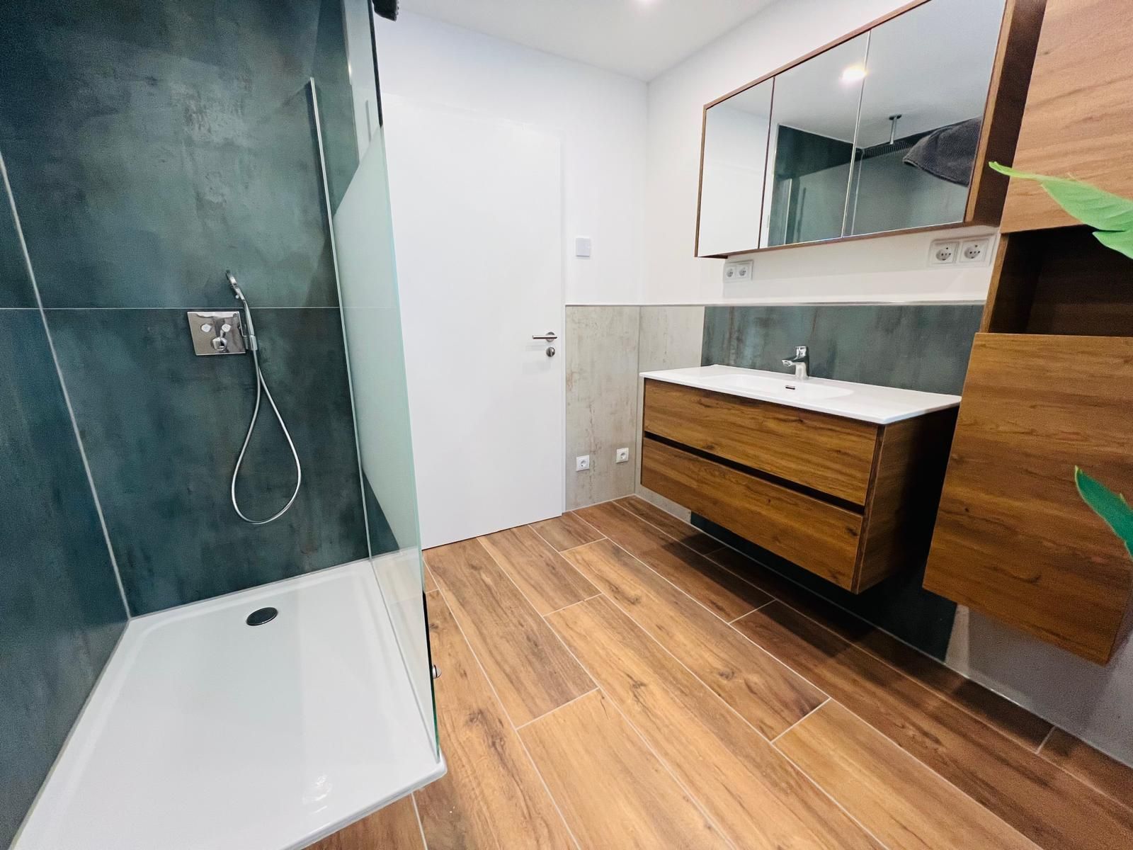 Modernes, geräumiges Bad mit bodengleicher Dusche, großflächigen Spiegeln und stilvollem Holzboden — für einen Monteur sehr komfortabel.