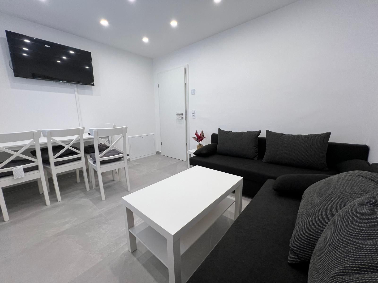 Modernes, helles Wohnzimmer mit funktional durchdachtem Layout – großes Sofa, TV, Esstisch und gute Beleuchtung bieten alles für komfortables Wohnen.
